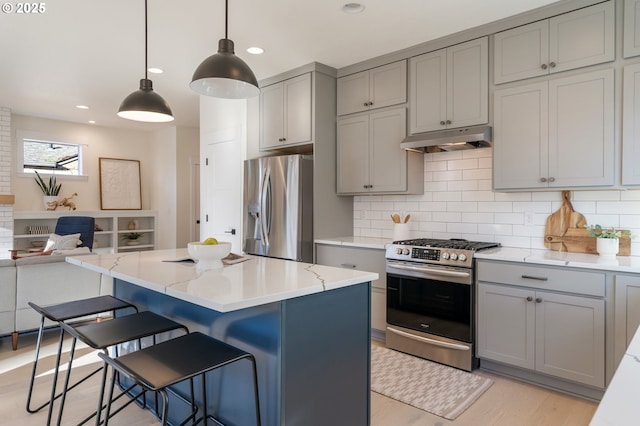 kitchen with a breakfast bar, open floor plan, hanging light fixtures, stainless steel appliances, and under cabinet range hood