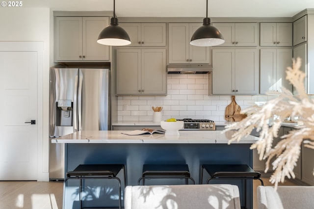 kitchen featuring hanging light fixtures, under cabinet range hood, light stone counters, and stainless steel refrigerator with ice dispenser