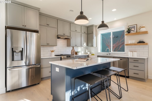 kitchen featuring light stone countertops, a center island, stainless steel appliances, light hardwood / wood-style floors, and a breakfast bar