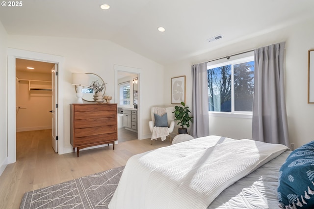 bedroom featuring a spacious closet, connected bathroom, light hardwood / wood-style floors, a closet, and lofted ceiling