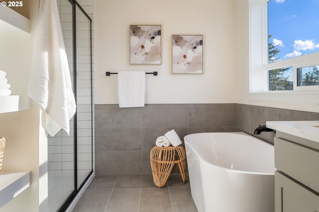 full bathroom with tile patterned flooring, vanity, tile walls, a freestanding bath, and a stall shower