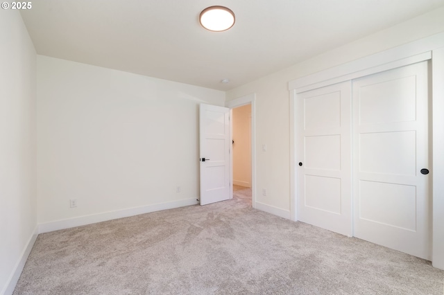 unfurnished bedroom with a closet, light colored carpet, and baseboards