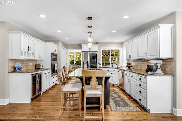 kitchen with white cabinetry, stainless steel appliances, wine cooler, dark stone countertops, and light hardwood / wood-style floors