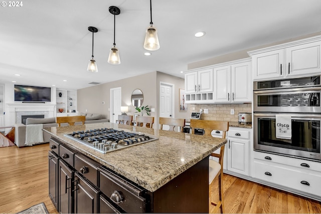 kitchen with a breakfast bar, stainless steel appliances, decorative light fixtures, light hardwood / wood-style flooring, and white cabinets