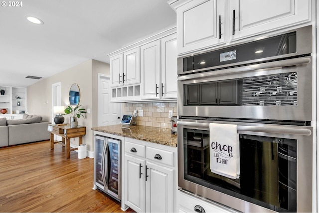 kitchen with white cabinets, stainless steel double oven, light hardwood / wood-style floors, and backsplash