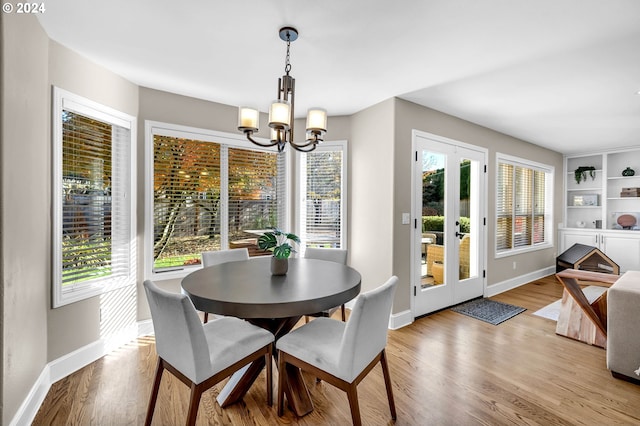 dining room featuring built in shelves, light wood-type flooring, french doors, and an inviting chandelier