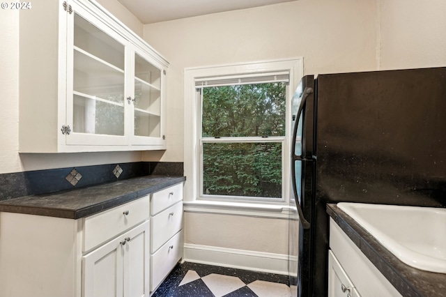 kitchen with black fridge, sink, and white cabinetry