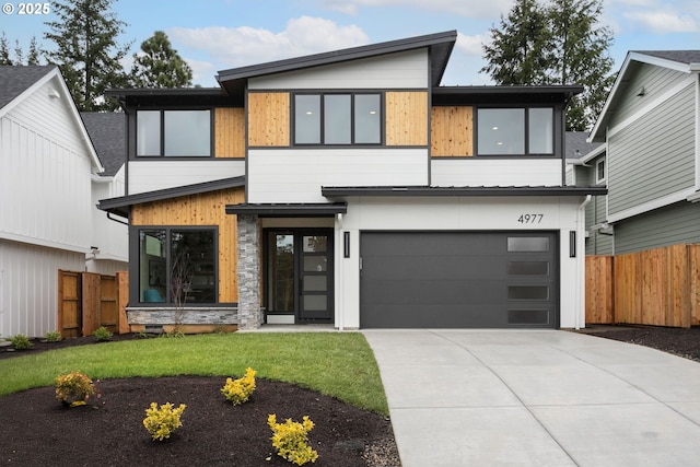 modern home with a front lawn, concrete driveway, an attached garage, and fence