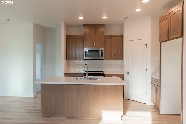 kitchen with tasteful backsplash, light hardwood / wood-style floors, a kitchen island with sink, and sink