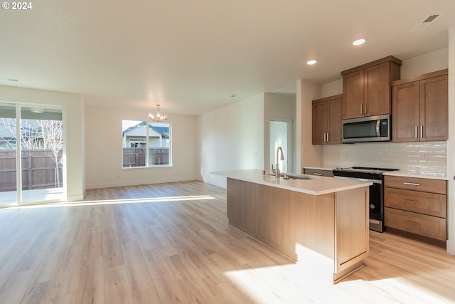 kitchen with sink, light wood-type flooring, an island with sink, appliances with stainless steel finishes, and a chandelier