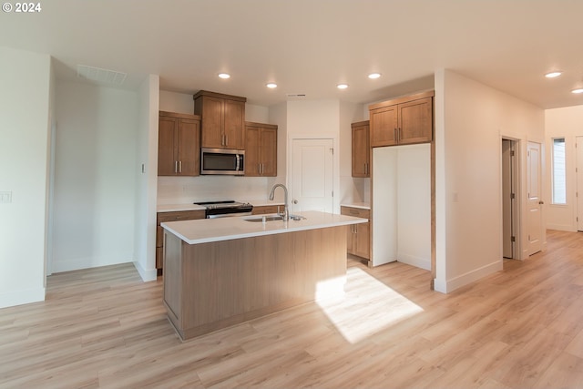 kitchen featuring sink, decorative backsplash, light wood-type flooring, an island with sink, and stainless steel appliances