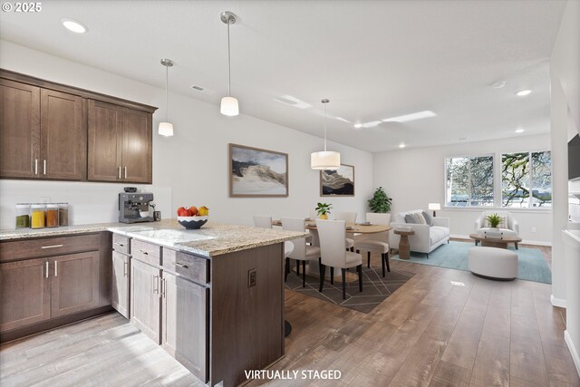 kitchen featuring dark brown cabinetry, light stone countertops, light wood-type flooring, decorative light fixtures, and kitchen peninsula