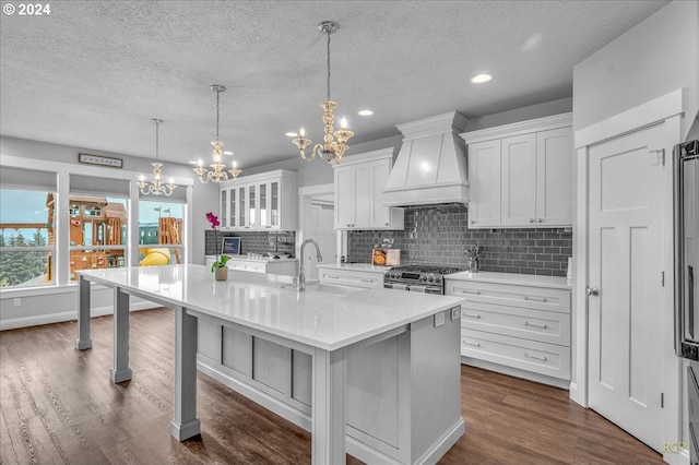 kitchen with gas range, custom range hood, a center island with sink, and white cabinets