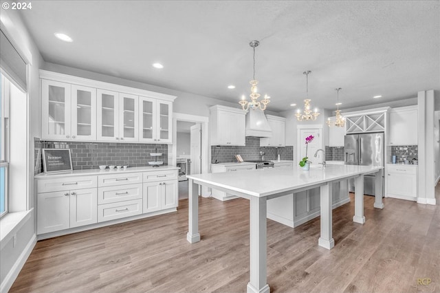 kitchen featuring a large island, premium range hood, appliances with stainless steel finishes, white cabinets, and decorative light fixtures