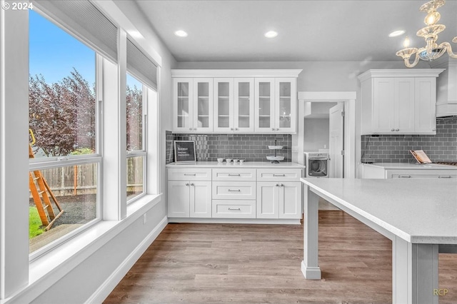 kitchen featuring washer / dryer, tasteful backsplash, hanging light fixtures, light hardwood / wood-style floors, and white cabinets