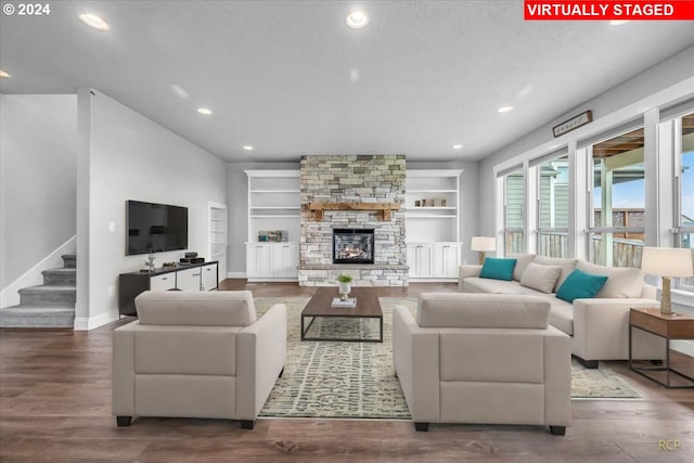 living room featuring built in features, a stone fireplace, hardwood / wood-style floors, and a textured ceiling