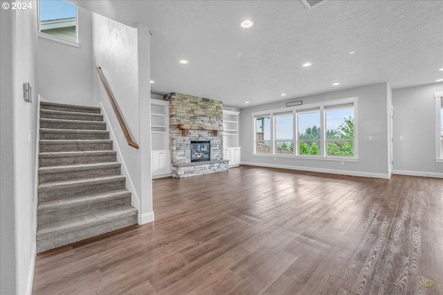 unfurnished living room with a fireplace, built in shelves, wood-type flooring, and a textured ceiling