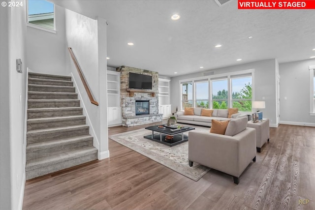 living room with built in shelves, a stone fireplace, hardwood / wood-style floors, and a textured ceiling