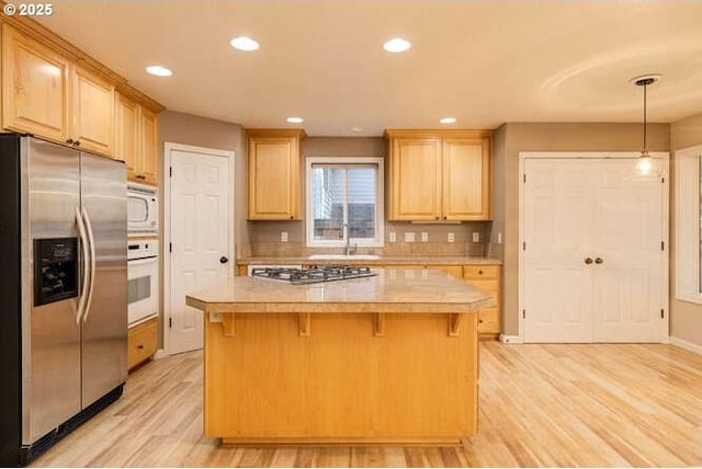 kitchen with light hardwood / wood-style flooring, appliances with stainless steel finishes, light brown cabinetry, and tile counters