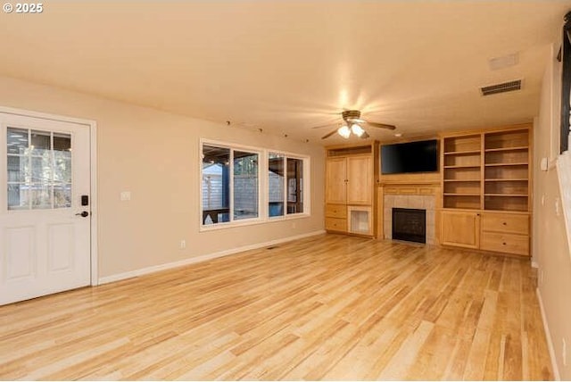 unfurnished living room featuring light hardwood / wood-style floors, built in features, a tile fireplace, and ceiling fan