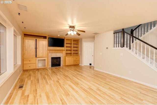 unfurnished living room featuring light hardwood / wood-style floors, a tile fireplace, built in features, and ceiling fan