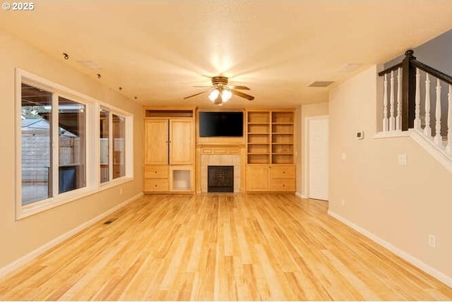 unfurnished living room featuring built in shelves, light hardwood / wood-style floors, a fireplace, and ceiling fan