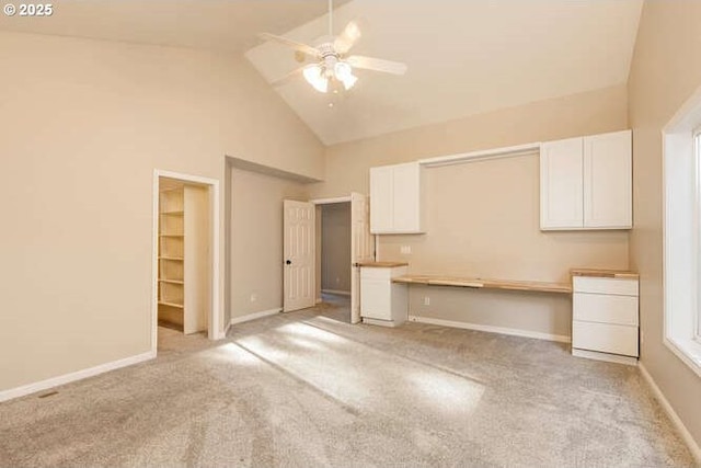 unfurnished living room with built in desk, high vaulted ceiling, ceiling fan, and light colored carpet