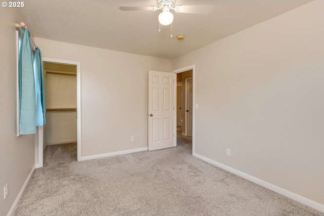 unfurnished bedroom with light colored carpet, a closet, ceiling fan, and a walk in closet