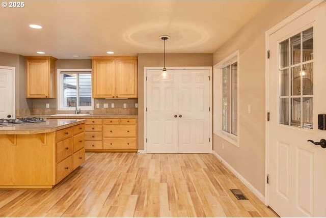 kitchen featuring a kitchen breakfast bar, light brown cabinets, pendant lighting, light wood-type flooring, and stainless steel gas cooktop