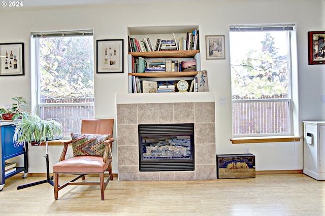 living area featuring a tiled fireplace, light wood-type flooring, and plenty of natural light