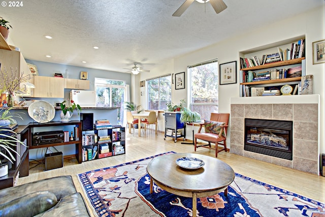 living room with light hardwood / wood-style floors, ceiling fan, a textured ceiling, and a tiled fireplace