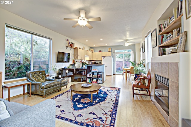 living room with a wealth of natural light, ceiling fan, a tile fireplace, and light hardwood / wood-style flooring