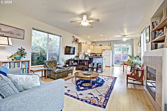 living room with ceiling fan, a wealth of natural light, a textured ceiling, and light hardwood / wood-style floors