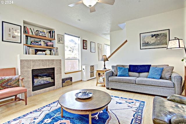 living room with ceiling fan, hardwood / wood-style flooring, a tiled fireplace, and a textured ceiling