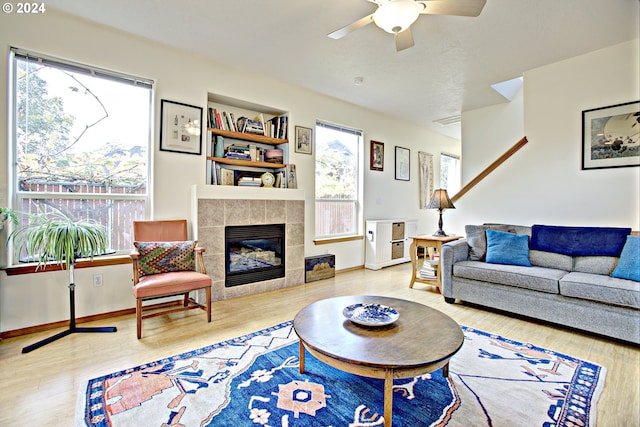 living room featuring a tiled fireplace, wood-type flooring, ceiling fan, and plenty of natural light