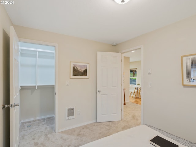 bedroom with heating unit, a spacious closet, light carpet, and a closet