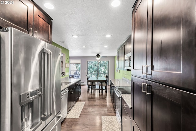 kitchen with dark brown cabinets, ceiling fan, stainless steel appliances, light stone counters, and dark hardwood / wood-style floors