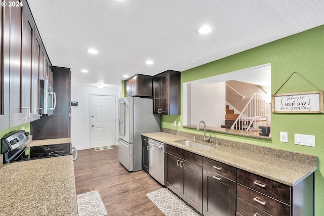 kitchen with dark brown cabinets, a textured ceiling, light hardwood / wood-style floors, appliances with stainless steel finishes, and sink