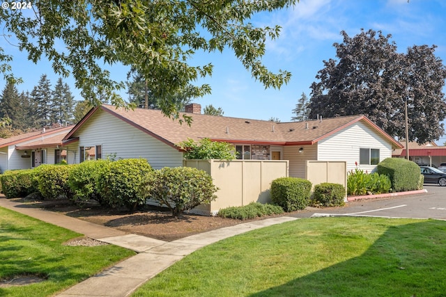 view of property exterior with fence, roof with shingles, a chimney, a yard, and uncovered parking