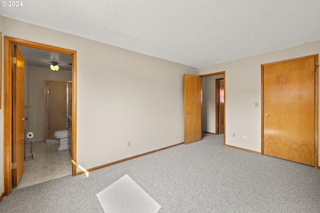 unfurnished bedroom featuring a textured ceiling, light colored carpet, and ensuite bath