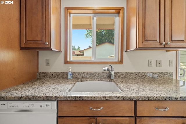 kitchen with light stone countertops, dishwasher, and sink