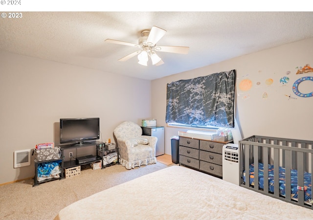 carpeted bedroom with fridge, ceiling fan, a nursery area, and a textured ceiling