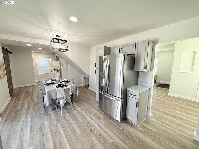 kitchen featuring a barn door, baseboards, light wood-style floors, gray cabinets, and stainless steel fridge with ice dispenser