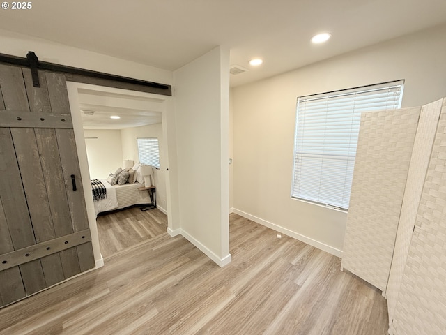 interior space featuring light wood finished floors, a barn door, baseboards, and recessed lighting