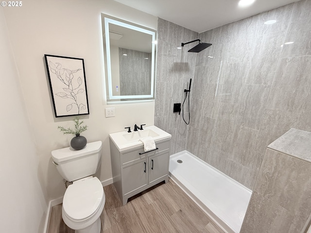 full bath featuring toilet, vanity, wood finished floors, tiled shower, and baseboards