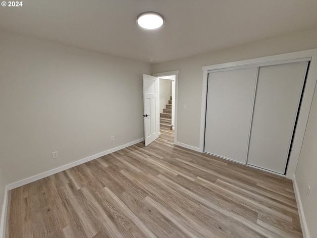 unfurnished bedroom featuring light wood finished floors, baseboards, and a closet