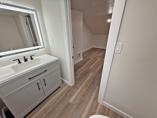 bathroom with baseboards, visible vents, wood finished floors, vaulted ceiling, and vanity