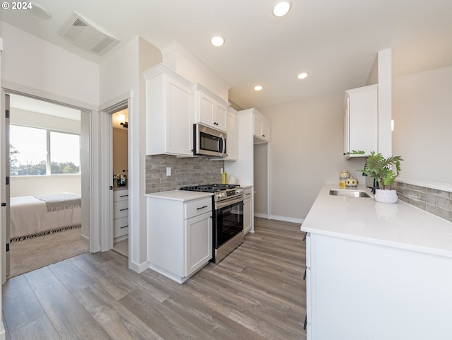 kitchen featuring decorative backsplash, stainless steel appliances, sink, white cabinets, and light hardwood / wood-style floors