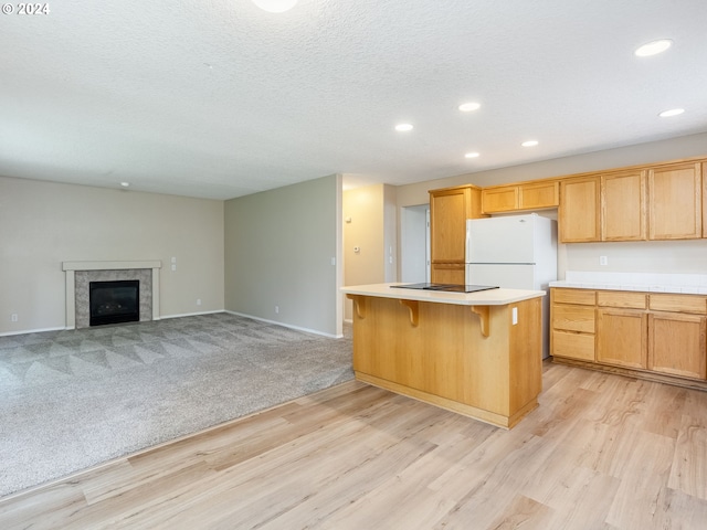 kitchen featuring a tiled fireplace, a textured ceiling, a kitchen bar, a kitchen island, and light colored carpet