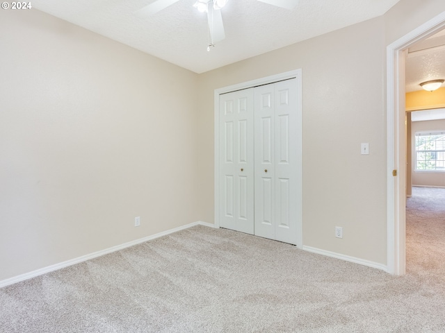 unfurnished bedroom with a textured ceiling, light colored carpet, ceiling fan, and a closet